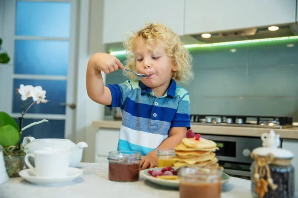 Маленький кудрявый мальчик ест сладкие блинчики — стоковое фото