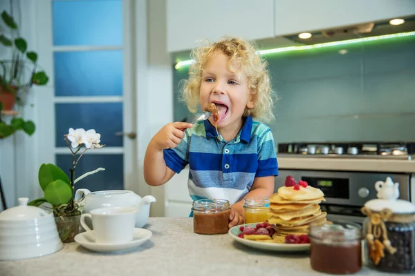 Маленький кудрявый мальчик ест сладкие блинчики — стоковое фото