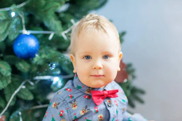 Malý chlapec v santa oblek hraje v blízkosti novoroční strom — Stock fotografie