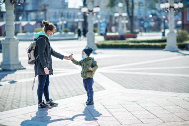Anne ve oğlu dışarıda maske takıp su içiyorlar.
