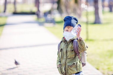 Maskeli bir çocuk elinde bir şişe su tutuyor.