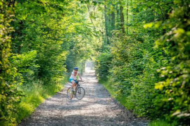 Güzel yeşil ormanda bisiklet süren bir kadın. Macera, bisiklet.