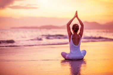 Kadın deniz kıyısında yoga yapıyor.