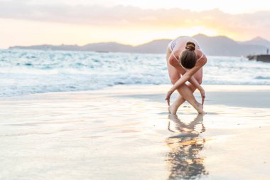 Kadın deniz kıyısında yoga yapıyor.