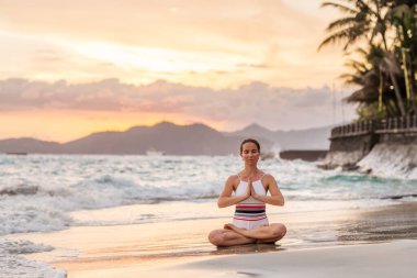 Kadın deniz kıyısında yoga yapıyor.