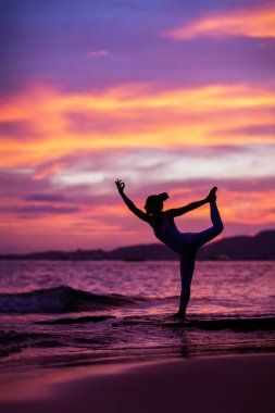 Kadın deniz kıyısında yoga yapıyor.