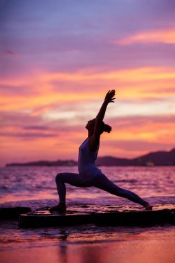 Kadın deniz kıyısında yoga yapıyor.