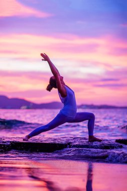 Kadın deniz kıyısında yoga yapıyor.