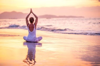 Kadın deniz kıyısında yoga yapıyor.