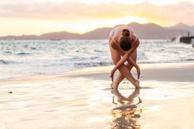 Kadın deniz kıyısında yoga yapıyor.