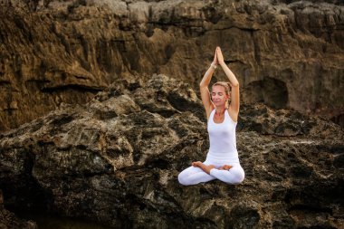 Kadın deniz kıyısında yoga yapıyor.