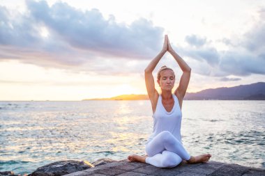 Kadın deniz kıyısında yoga yapıyor.