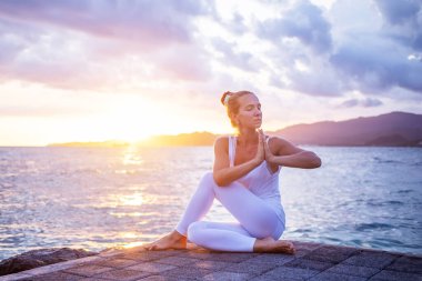 Kadın deniz kıyısında yoga yapıyor.