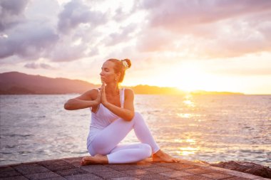 Kadın deniz kıyısında yoga yapıyor.