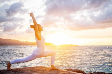 Kadın deniz kıyısında yoga yapıyor.