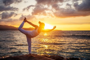 Kadın deniz kıyısında yoga yapıyor.