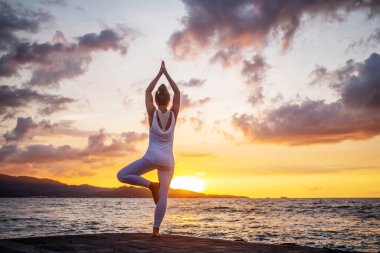 Kadın deniz kıyısında yoga yapıyor.
