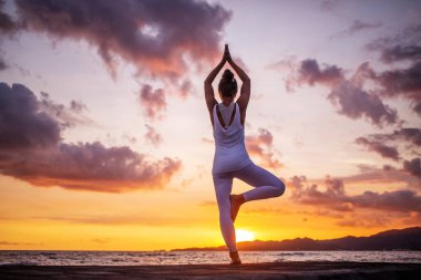 Kadın deniz kıyısında yoga yapıyor.
