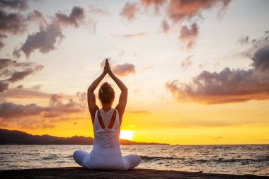 Kadın deniz kıyısında yoga yapıyor.