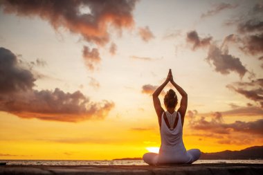 Kadın deniz kıyısında yoga yapıyor.