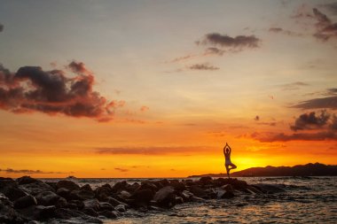 Kadın deniz kıyısında yoga yapıyor.