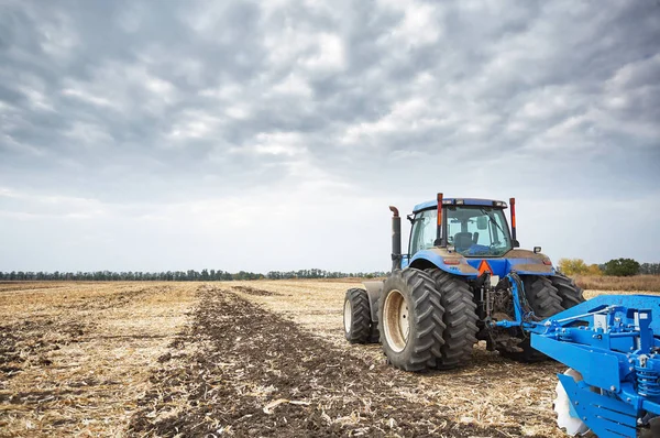 Traktor med plov arbejder i marken - Stock-foto
