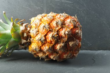 Olgun ananas meyvesi gri levhada yatıyor.