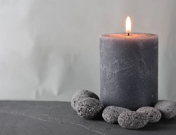 A gray wax candle surrounded by pebbles — Stock Photo, Image