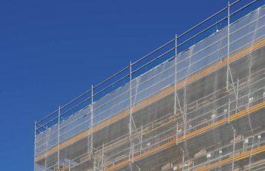 Tadilat altındaki bir binanın iskelesi beyaz güvenlik ağıyla çevrili.