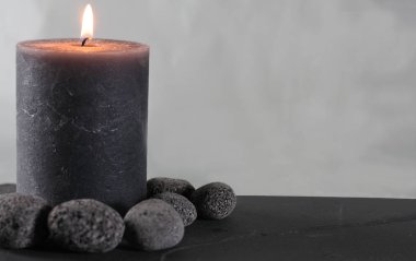 Koyu çakıl taşlarıyla çevrili bir levhada gri bir mum.