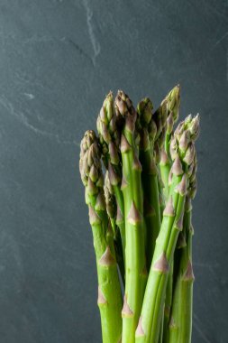 Yeşil kuşkonmaz demetine yakın çekim, arka planda gri bir arkaplan oluşturur.