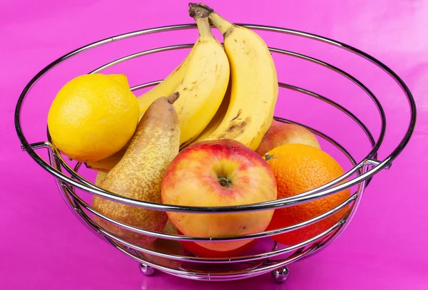 a variety of fruits in a steel basket on pink background