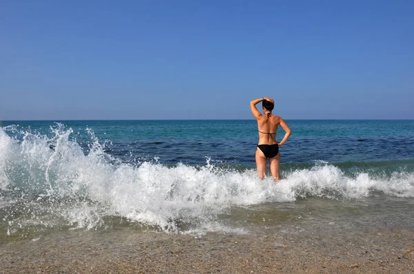 Genç güzel kadın. Siyah mayo giyen bir kadın deniz dalgalarında yürümekten hoşlanır ve güneşlenir.