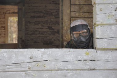 Aktif paintball oyunu. Koruyucu üniformalı ve maskeli bir paintball oyuncusu eski bir evde pusuda bekliyor..