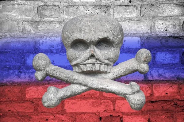 Totenkopf und Kreuzknochen an einer alten Ziegelwand, die in den Farben der Flagge Russlands bemalt ist. Konzept bringt den Tod — Stockfoto