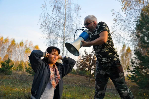 Ein Mann brüllt eine Frau im Wald durch ein Megafon an. schreien Sie Ihren Liebsten zu. Häusliche Gewalt. — Stockfoto