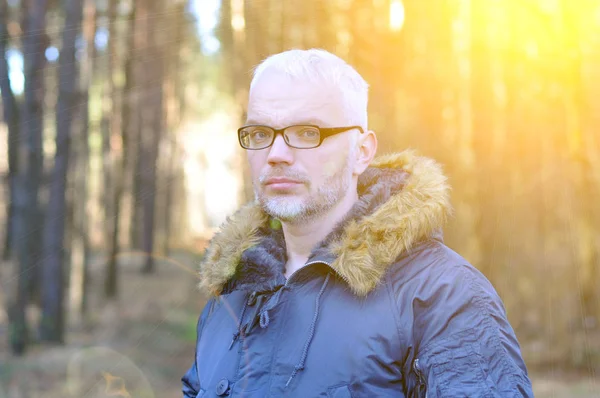 Close-up portret van een intelligente man met grijs haar en glazen, een baard in de warme winter tegen de achtergrond van het bos. Verrassing. — Stockfoto