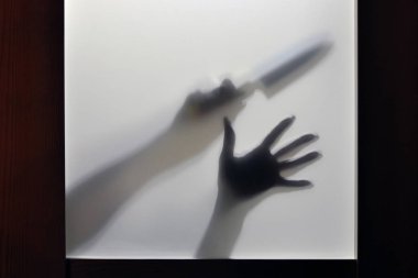 The concept of domestic violence in the family. Hand with a knife, shadows through the door glass.