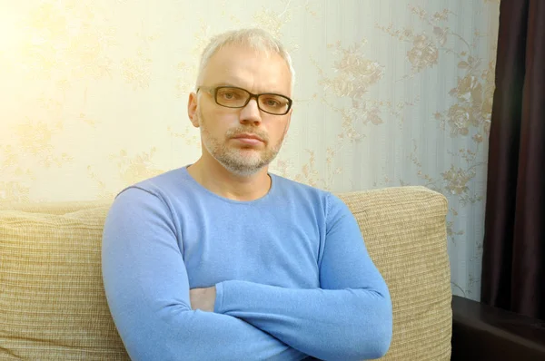 Przystojny młody mężczyzna w niebieskim swetrze i okularach siedzi i patrzy w kamerę. Zbliżenie — Zdjęcie stockowe