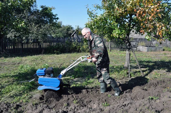 Das Land im Garten mit einem Grubber pflügen. Ein Mann pflügt das Land mit Hilfe eines Motorbootes. — Stockfoto