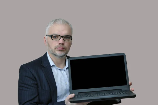 Homme d'affaires dans des lunettes et avec une barbe tient un ordinateur portable avec un écran blanc . — Photo
