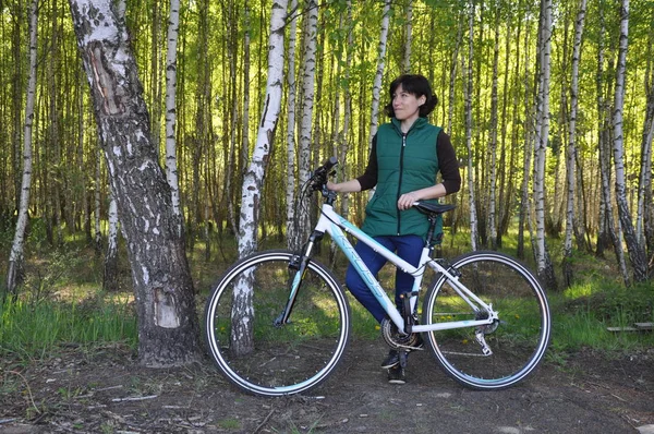 Hermosa mujer joven En una bicicleta de pie en el bosque contra el telón de fondo de un abedul. acondicionamiento físico — Foto de Stock