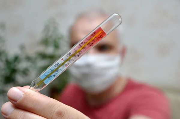 A mercury thermometer indicating a high temperature is in the hands of a sick man. The man is out of focus.
