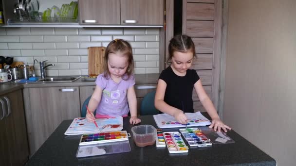 Duas meninas irmãs pintam com pinturas infantis em uma mesa na cozinha — Vídeo de Stock