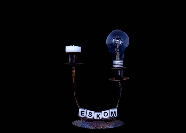 Mum tutucu, sönük bir elektrik ampulü ve Eskom terimi yatay formatında fotokopi alanı olan siyah bir arkaplan resmi üzerinde izole edilmiş.