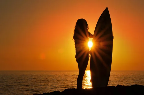Silueta ženy na pobřeží drží surfovací prkno při západu slunce — Stock fotografie