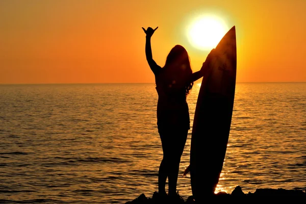Siluett kvinna på kusten håller surfbräda i solnedgången — Stockfoto