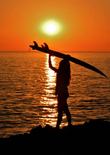 Silueta mujer en costa celebración de tabla de surf al atardecer — Foto de Stock