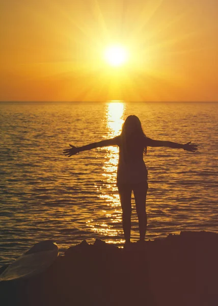 Flicka med avslappnad öppna armar ser ut på havet i solnedgången — Stockfoto