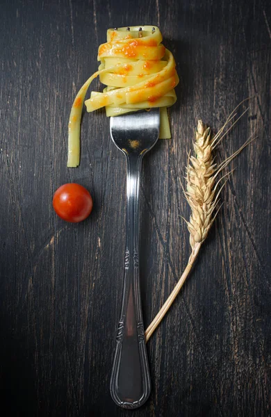 Widelec z fettuccine z pomidorem na dojrzałym czarnym drewnianym stole — Zdjęcie stockowe